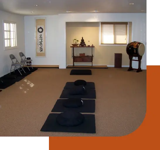 The ZCOC Main Zendo, with cushions and chairs in rows, an alcove with altar featuring ikebana floral arrangement and Buddha statue
